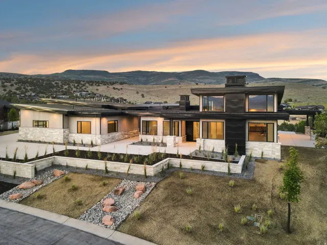 Modern architectural design featuring expansive windows, natural stone accents, a multi-level exterior, and structured landscaping with rock features