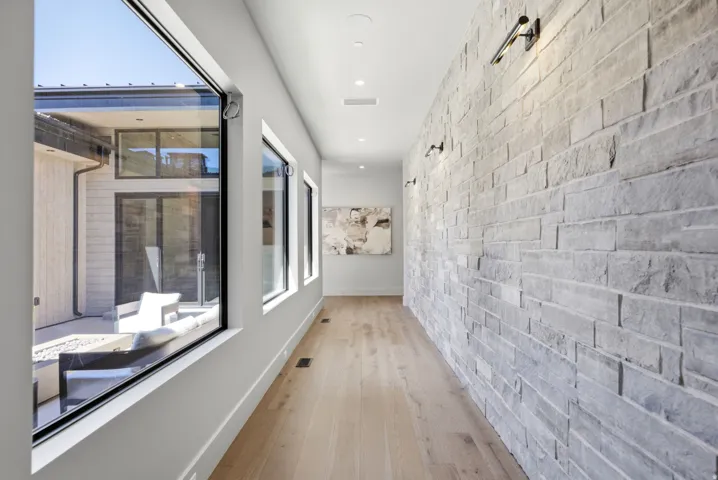 Expansive stone accent wall featuring wall-mounted sconces, light wood-finish flooring, recessed ceiling lighting, and multiple large windows with black frames