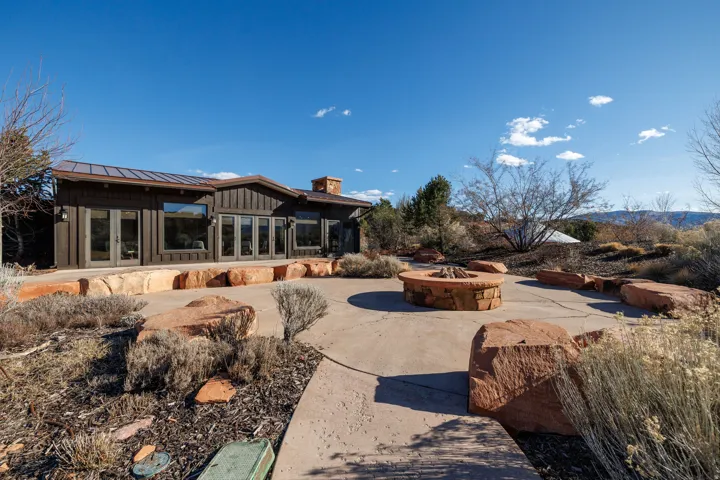 Exterior featuring multiple sets of French doors, an outdoor fire pit with stone surround, a concrete patio, and natural rock landscaping elements