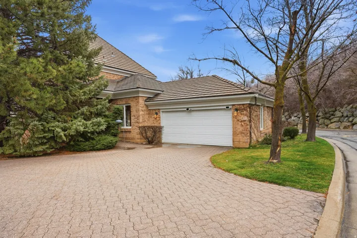View of property exterior featuring brick siding, decorative driveway, an attached garage, a tiled roof, and a lawn