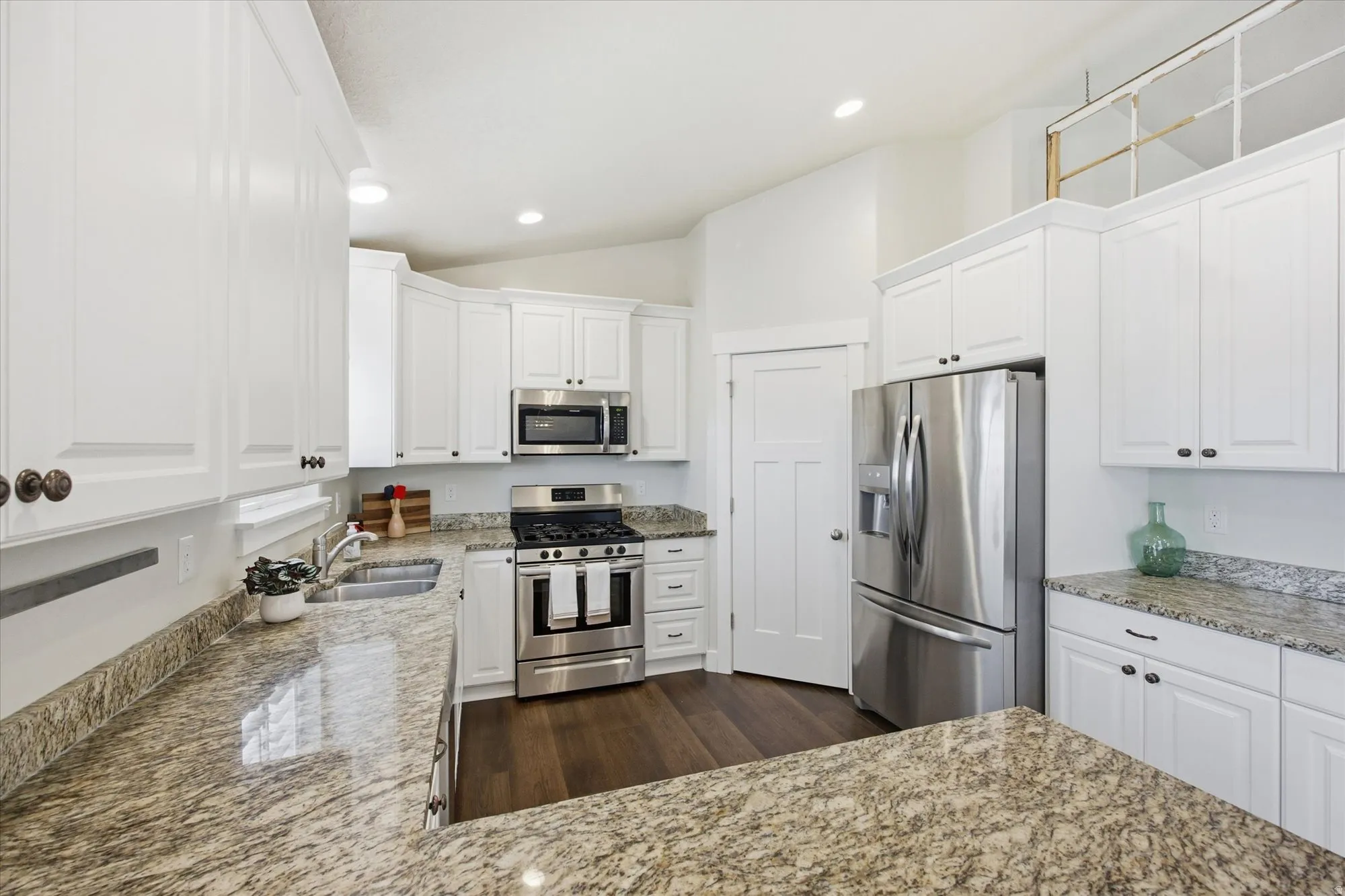 Kitchen featuring white cabinetry, stainless steel appliances, lofted ceiling, light stone countertops, and recessed lighting