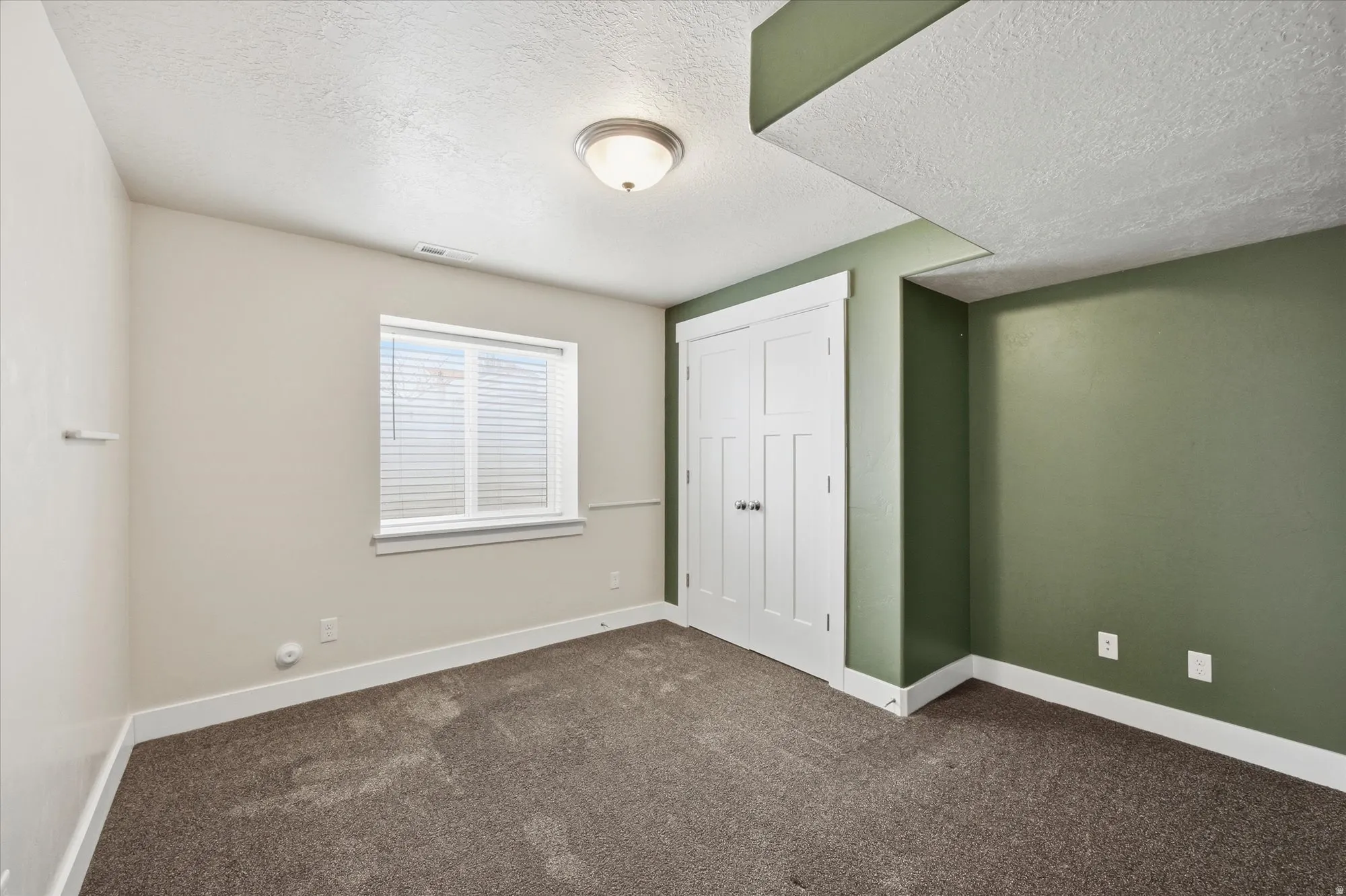 Unfurnished bedroom featuring dark colored carpet, a textured ceiling, and a closet