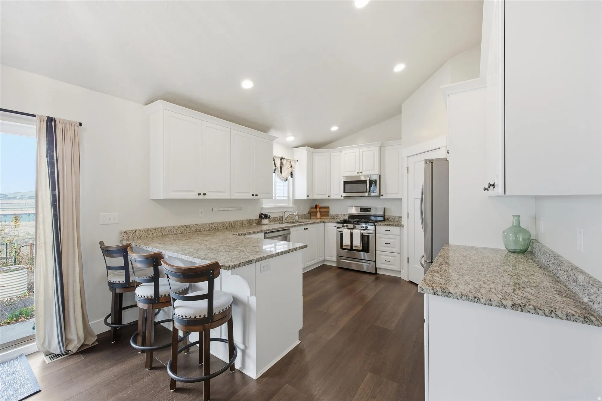 Kitchen with stainless steel appliances, white cabinetry, dark wood-type flooring, a kitchen breakfast bar, and vaulted ceiling