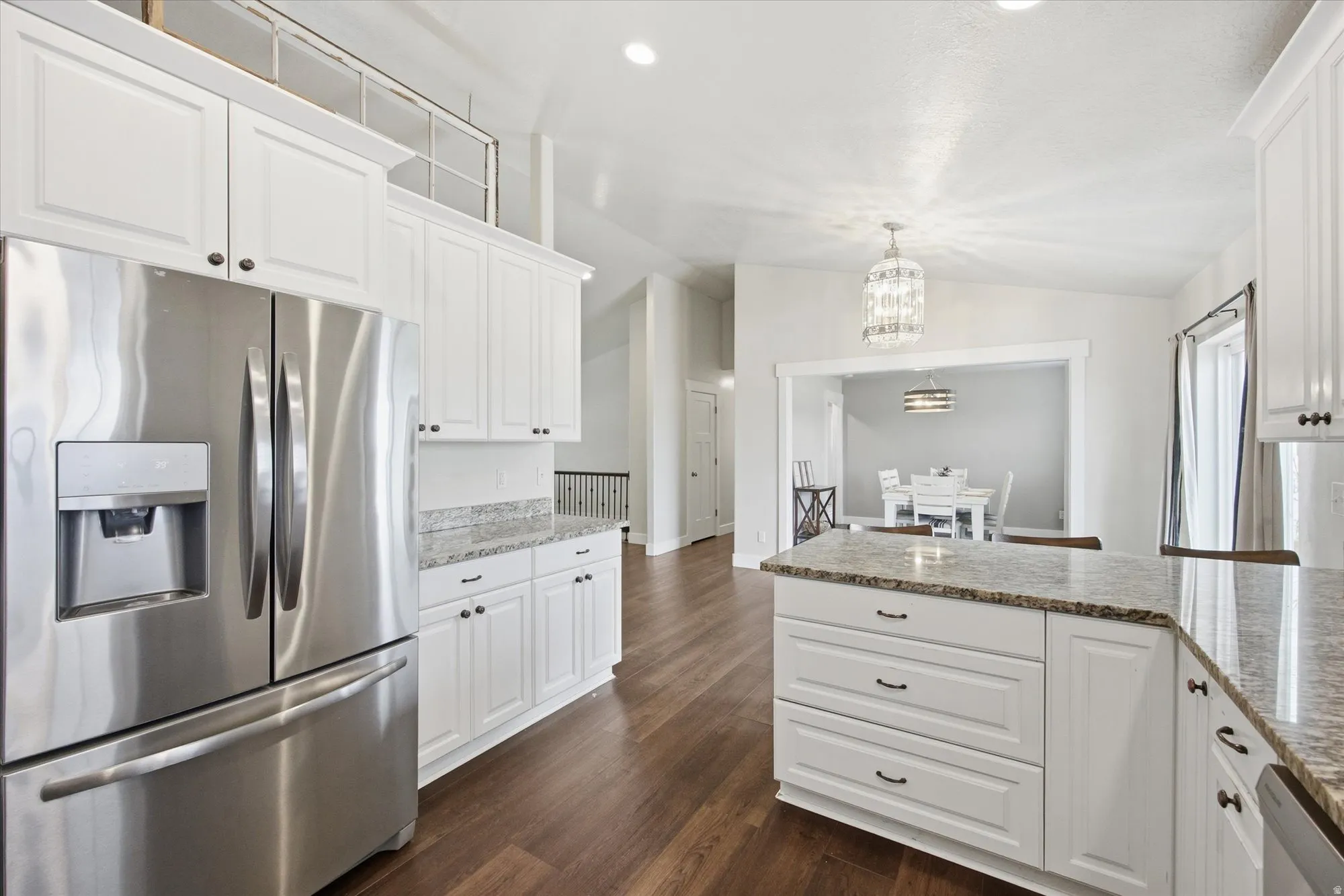 Kitchen with stainless steel appliances, white cabinetry, dark wood-style floors, and vaulted ceiling