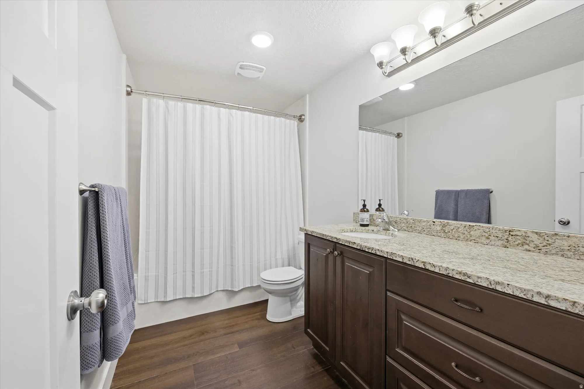 Bathroom featuring vanity, dark wood-style floors, shower / bath combo, and a textured ceiling