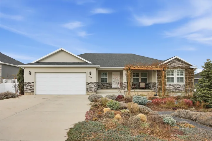 Ranch-style house featuring an attached garage, driveway, stucco siding, a porch, and stone siding.  MARCH