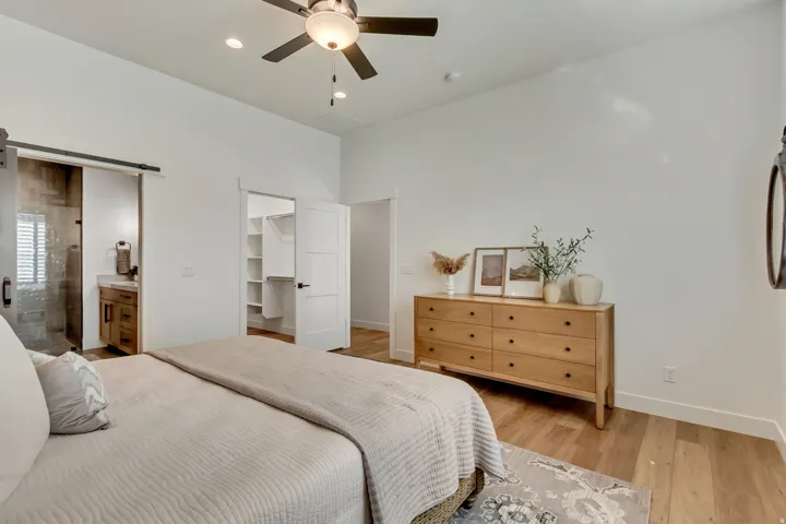 Bedroom with a barn door, a walk in closet, light wood-style floors, a ceiling fan, and connected bathroom