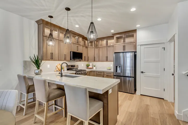 Kitchen with a peninsula, stainless steel appliances, a kitchen breakfast bar, light wood finished floors, and glass fronted cabinets