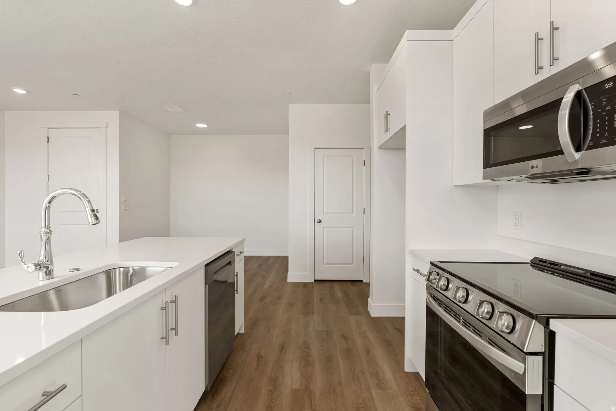 Kitchen featuring stainless steel appliances, white cabinets, dark wood finished floors, light stone counters, and recessed lighting