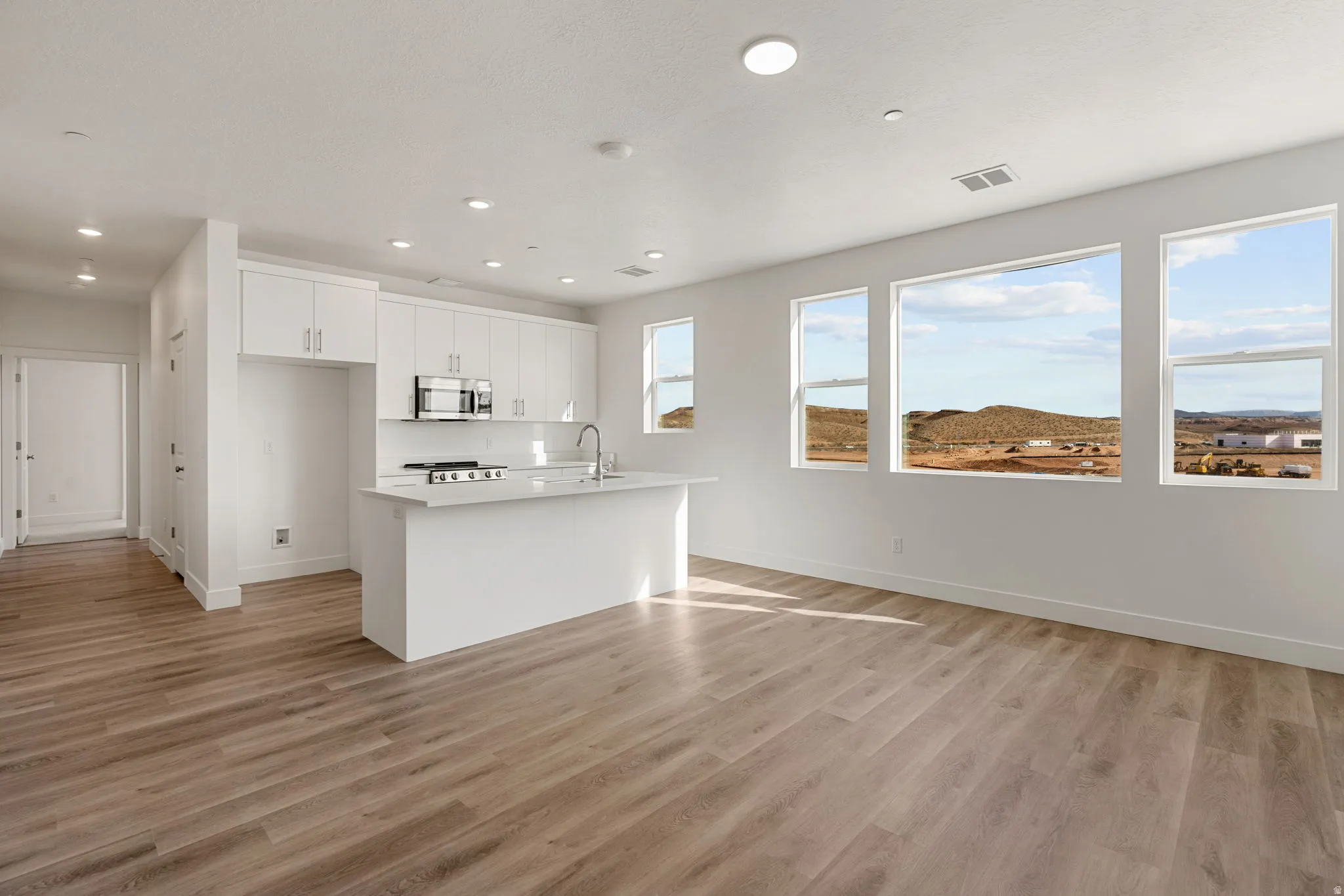 Kitchen with light countertops, a center island with sink, white cabinetry, light wood-type flooring, and stainless steel microwave