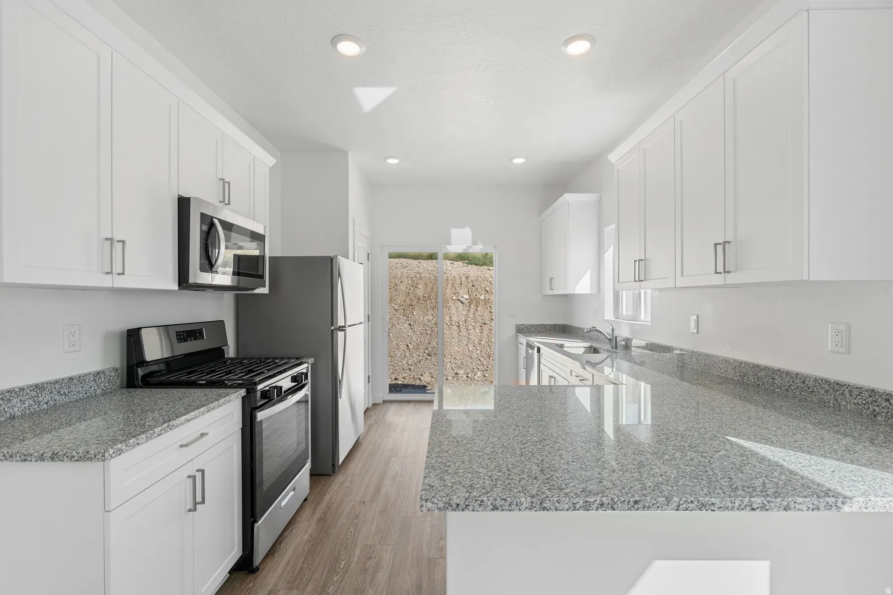 Kitchen with light stone counters, white cabinets, stainless steel appliances, a peninsula, and recessed lighting