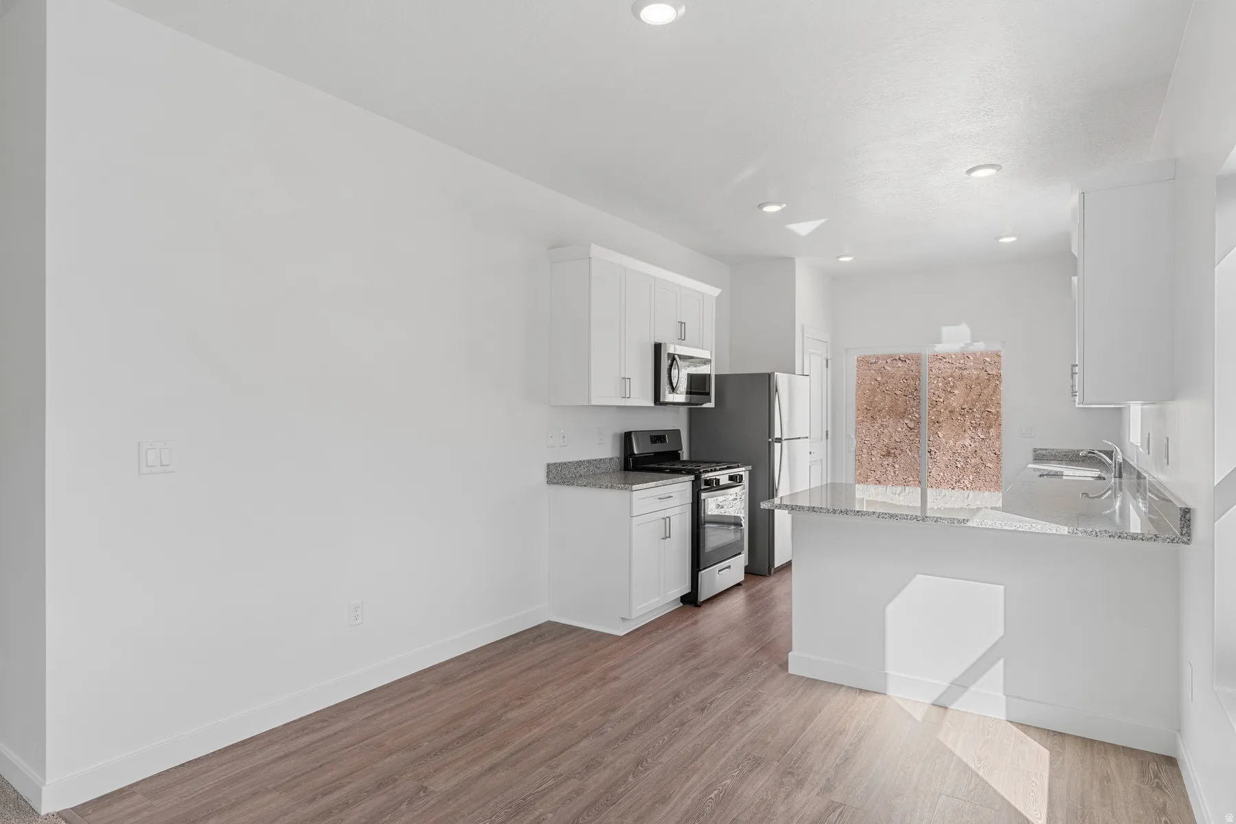 Kitchen with white cabinets, stainless steel appliances, light stone counters, light wood-style floors, and a peninsula
