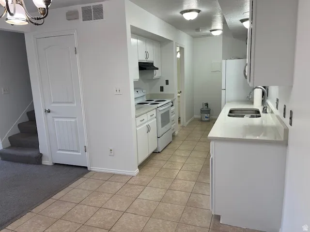 Kitchen featuring white range with electric stovetop, white cabinets, light tile patterned flooring, light carpet, and a chandelier