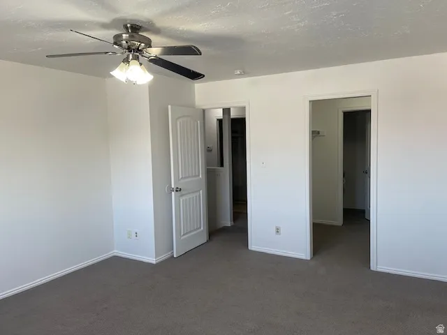 Unfurnished bedroom featuring dark carpet, a ceiling fan, and a textured ceiling