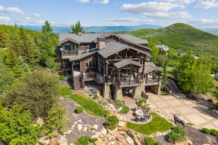 Rear view of house featuring a deck with mountain view, a standing seam roof, stone siding, driveway, and outdoor dining area