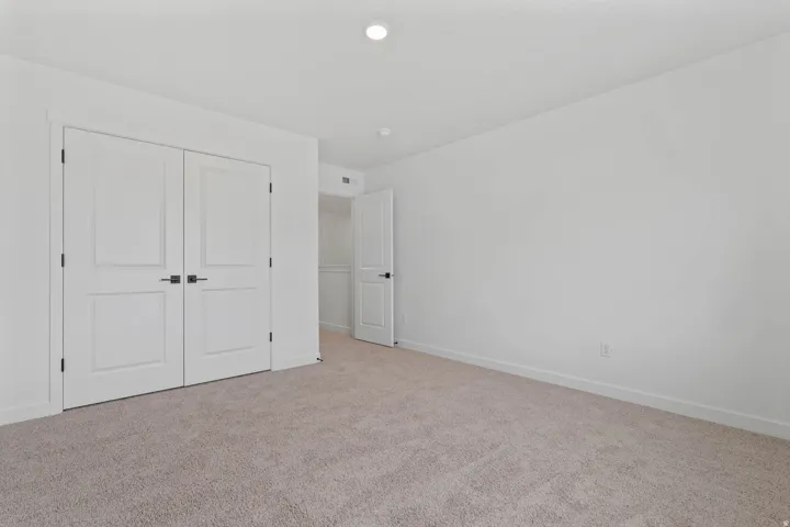 Neutral tone wall finish, plush carpet flooring, recessed ceiling light, white baseboards, and double closet doors with dark hardware