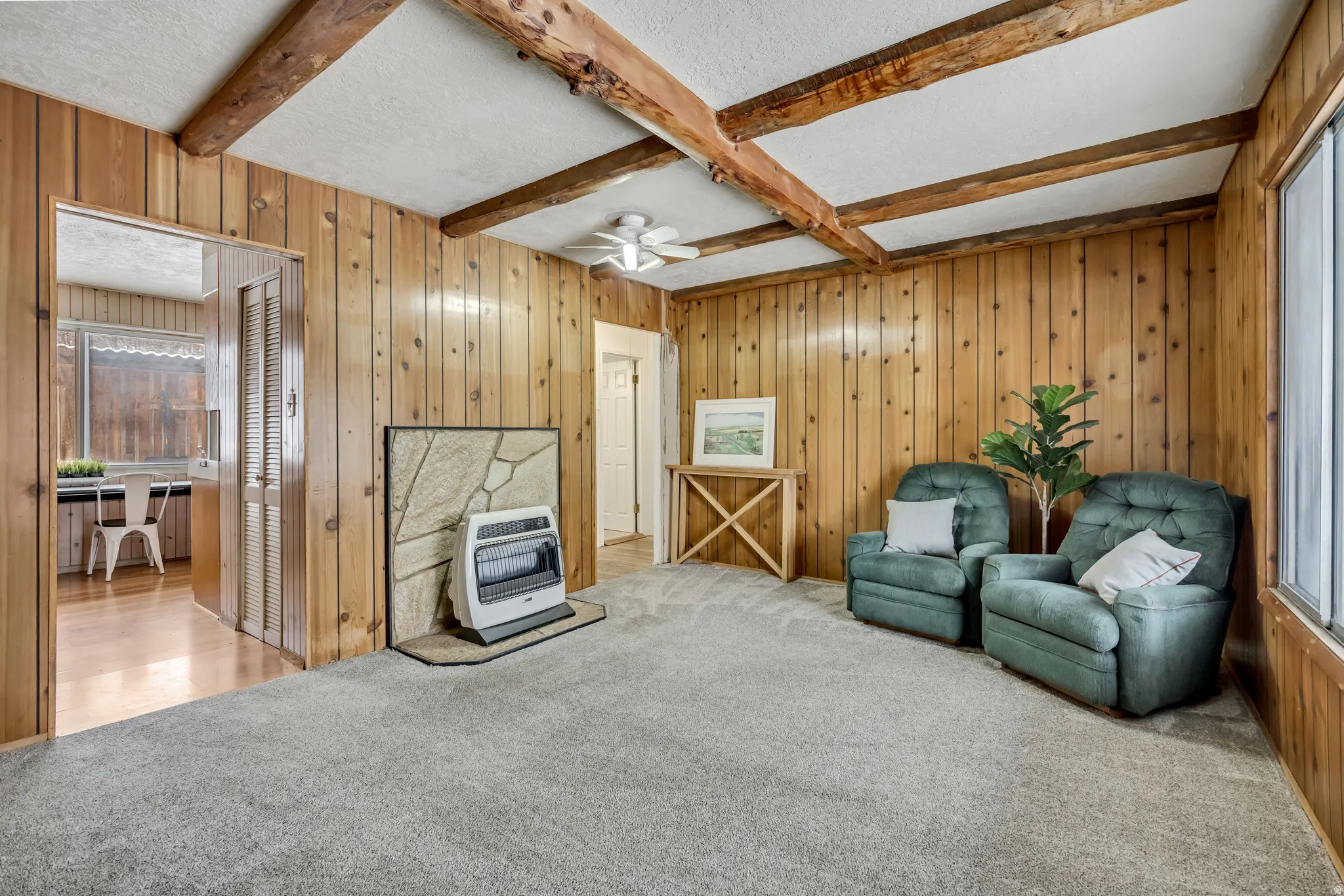 Sitting room with a textured ceiling, wood walls, carpet, beam ceiling, and a ceiling fan