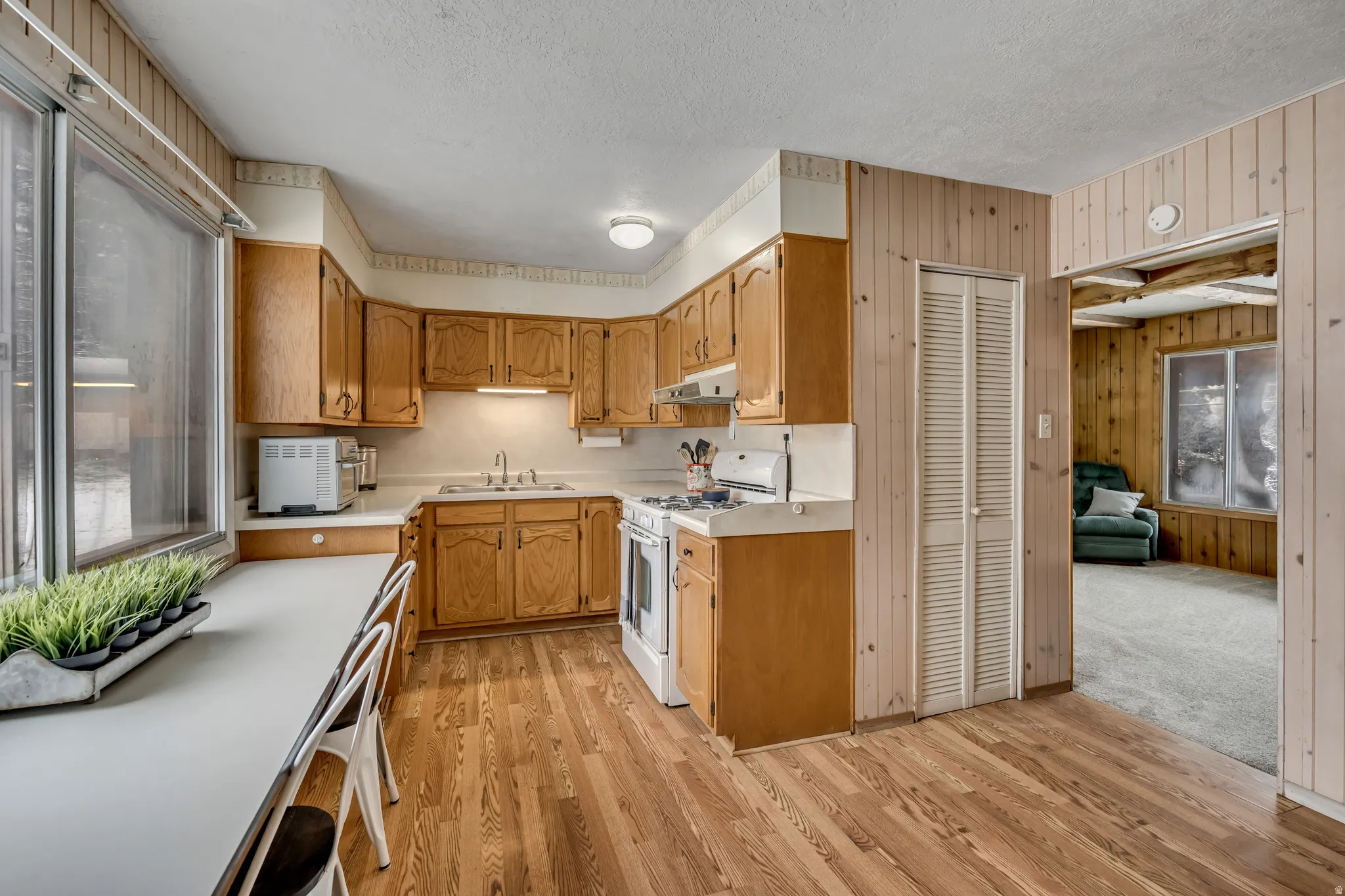 Kitchen featuring light countertops, white range with gas cooktop, a textured ceiling, light wood-style floors, and wooden walls