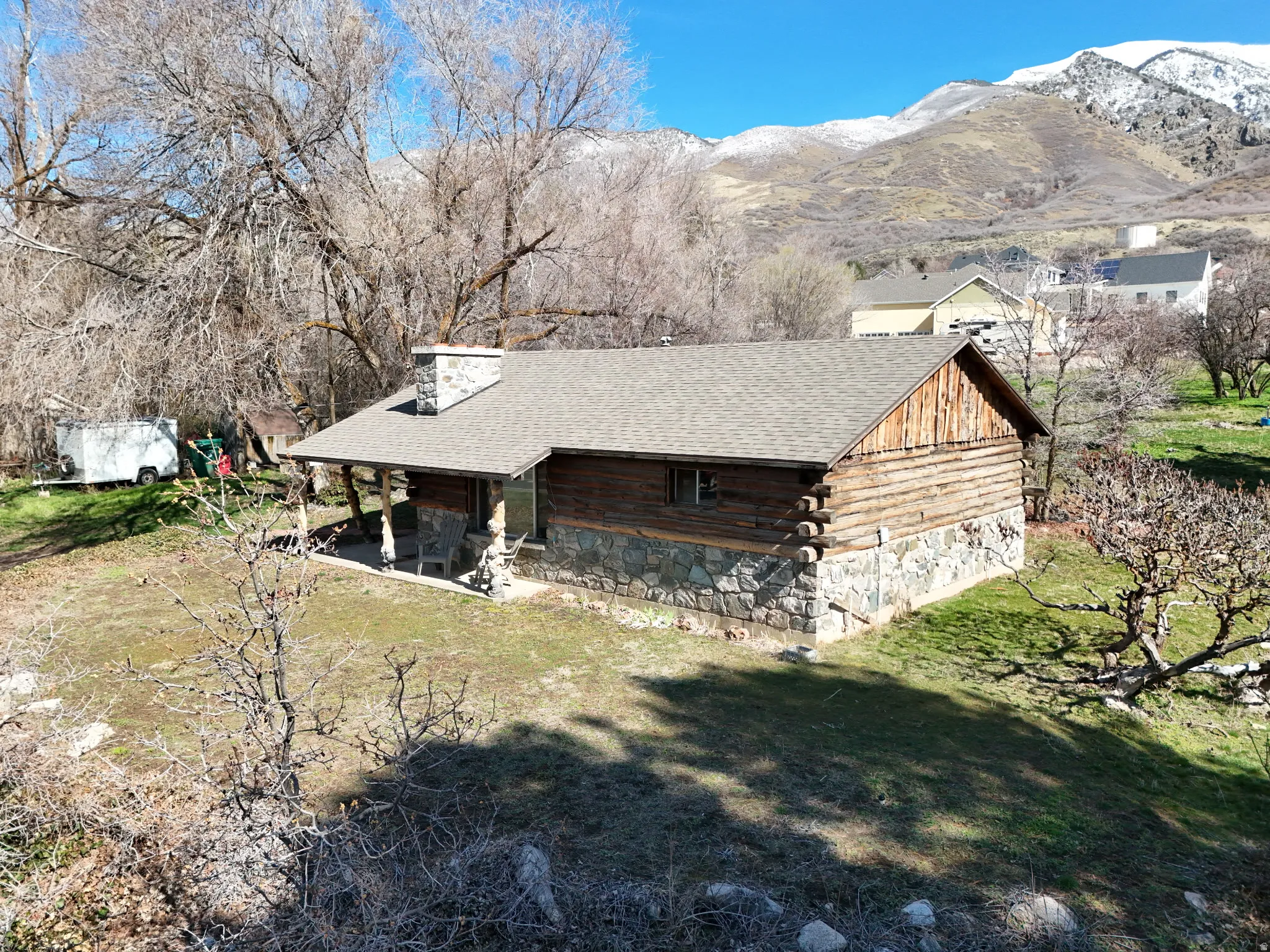 View of home's exterior featuring a shingled roof, log siding, a lawn, and a mountain view