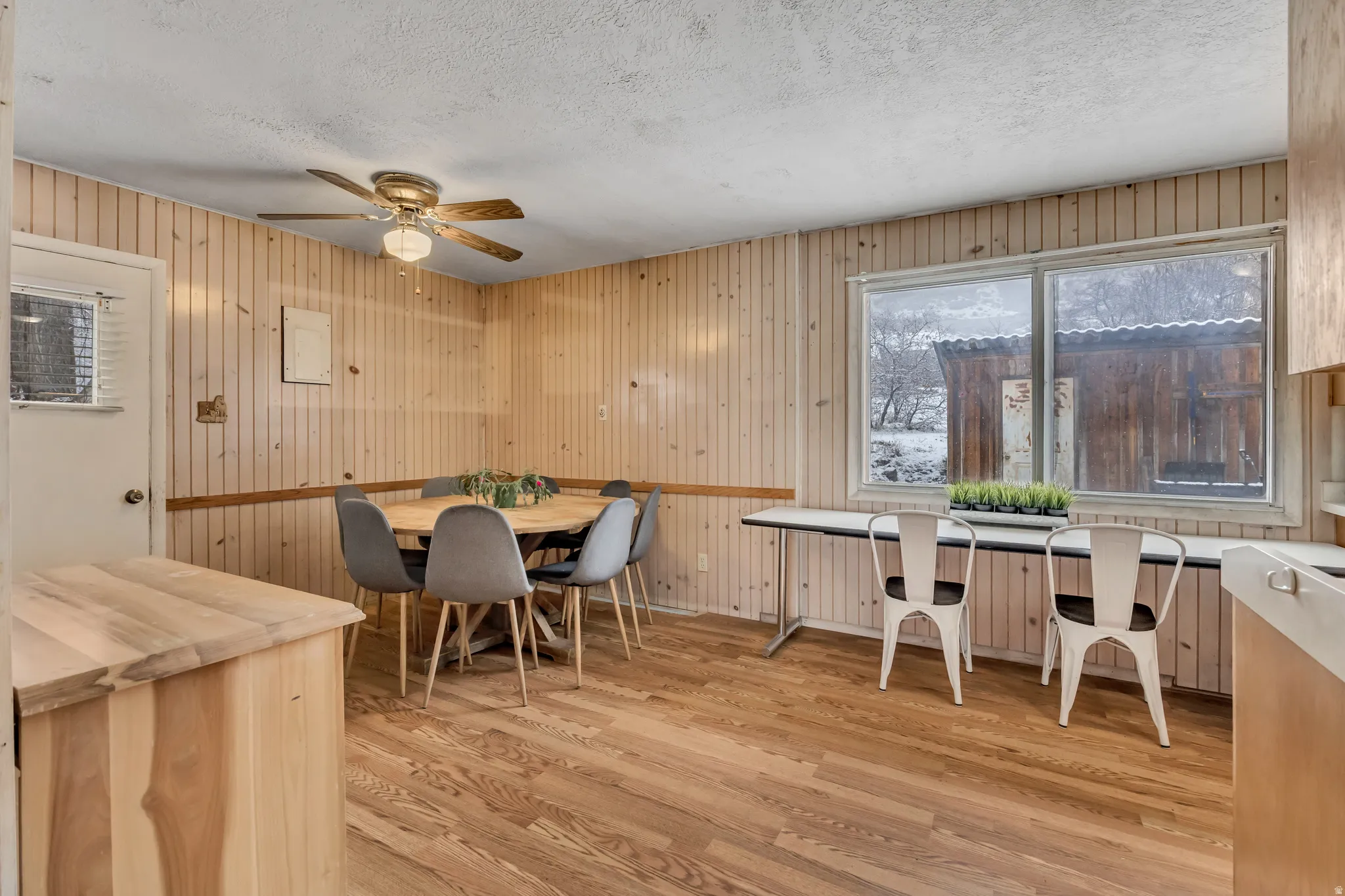 Dining room featuring light wood-type flooring, ceiling fan, wood walls, and a textured ceiling