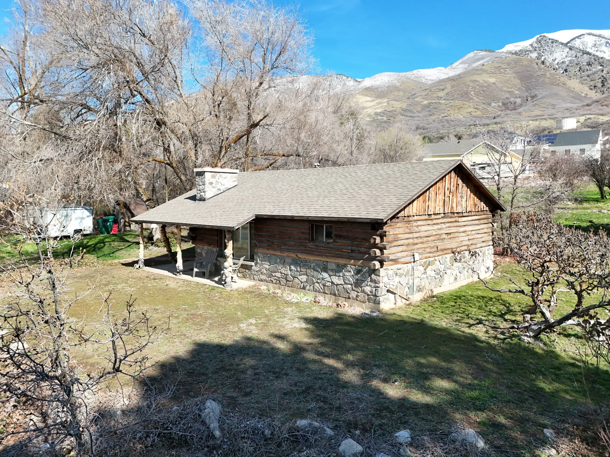 View of side of home with a lawn, a shingled roof, log siding, and a patio area