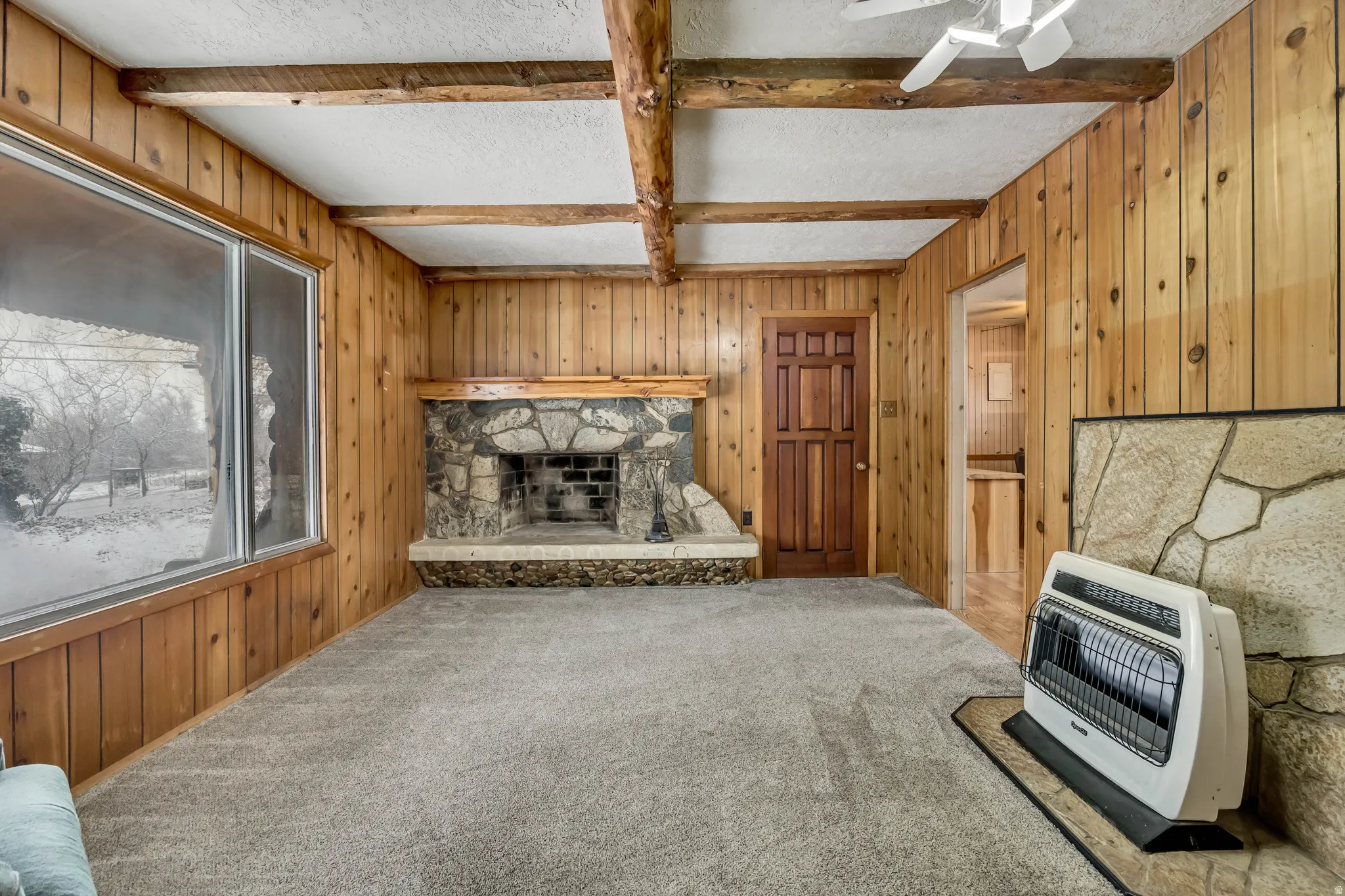 Unfurnished living room with wood walls, heating unit, carpet floors, a fireplace, and beamed ceiling