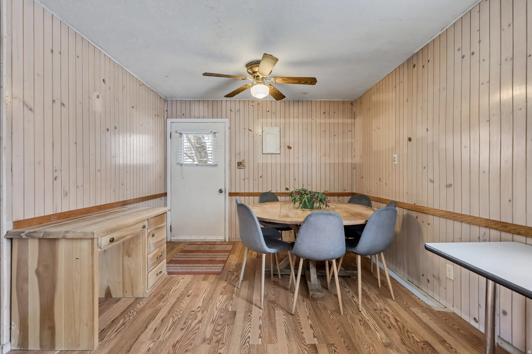 Dining room with light wood-style flooring, wooden walls, and ceiling fan