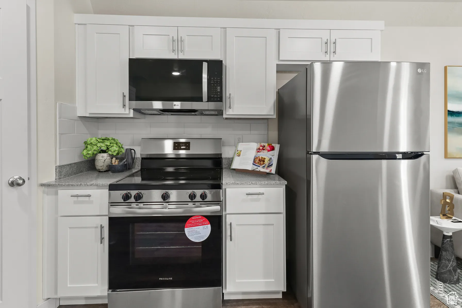 Kitchen with stainless steel appliances, white cabinetry, light stone countertops, and decorative backsplash