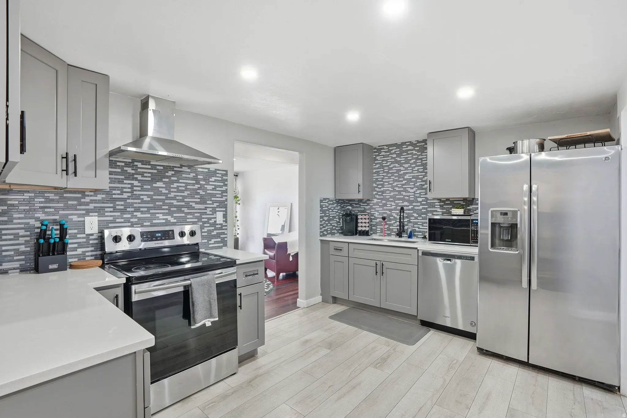Kitchen featuring gray cabinets, stainless steel appliances, light wood finished floors, light stone countertops, and recessed lighting