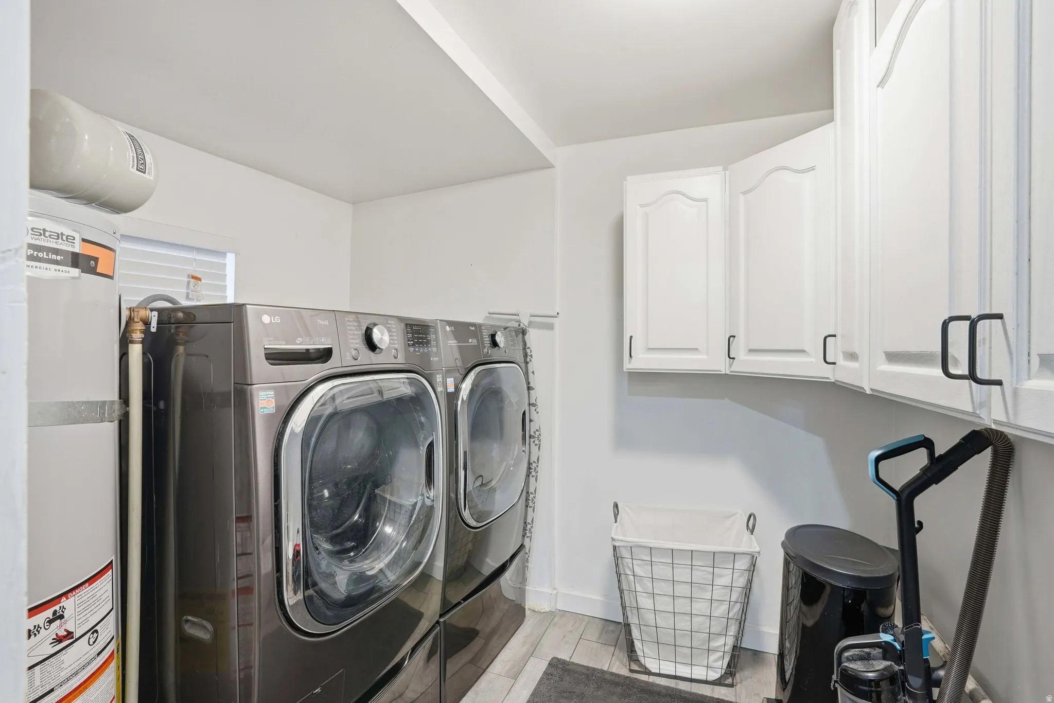 Laundry room with water heater, light wood-type flooring, cabinet space, and washing machine and dryer