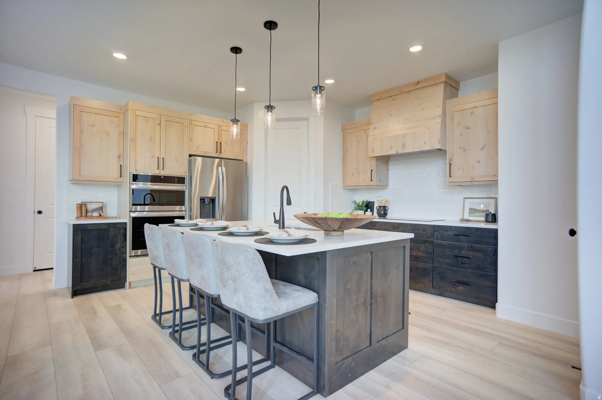 Kitchen with light wood finish cabinetry, stainless steel appliances, a breakfast bar area, light wood finished floors, and a kitchen island with sink