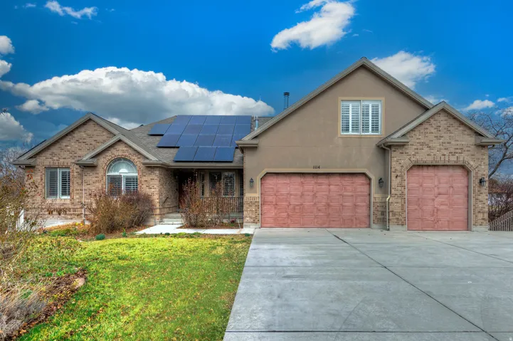 View of front facade featuring roof mounted solar panels, driveway, a front yard, brick siding, and stucco siding