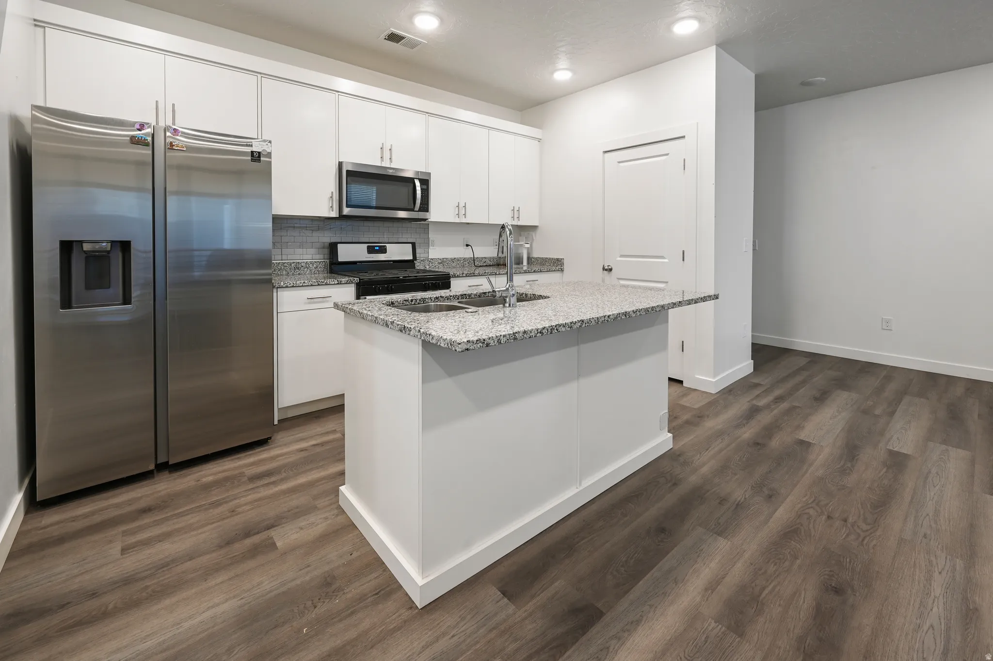 Kitchen with stainless steel appliances, white cabinets, a kitchen island with sink, decorative backsplash, and dark wood-type flooring