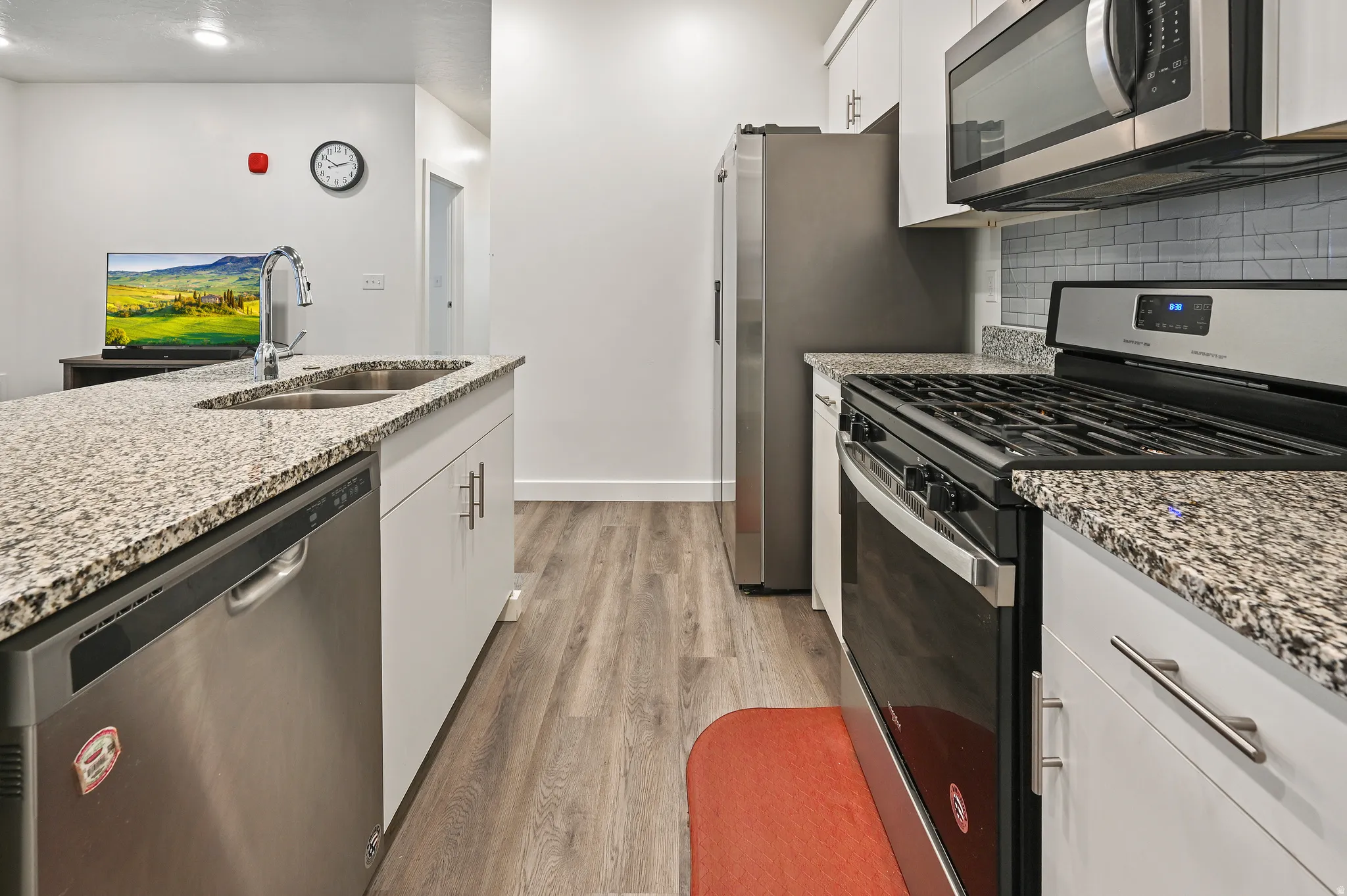 Kitchen featuring stainless steel appliances, light stone countertops, light wood-style flooring, white cabinetry, and tasteful backsplash