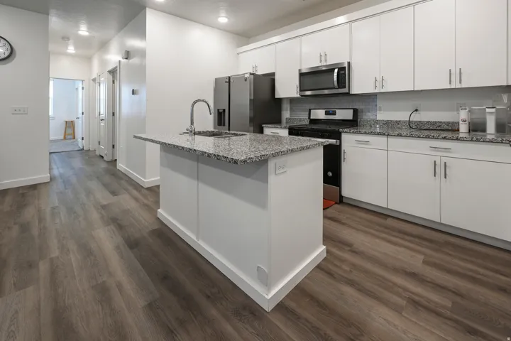 Kitchen featuring stainless steel appliances, white cabinetry, a center island with sink, and dark wood-style floors