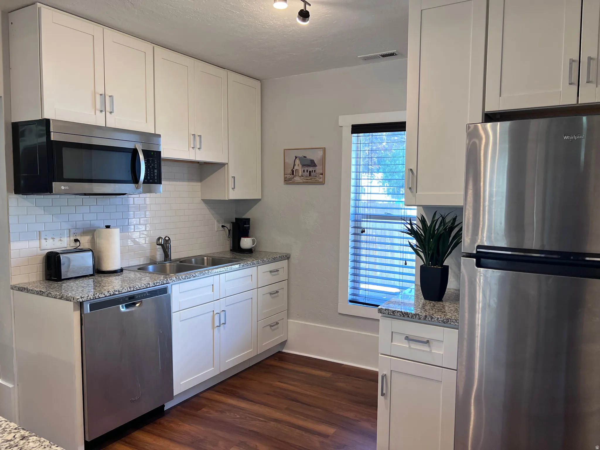 Kitchen with stainless steel appliances, light stone countertops, white cabinetry, and a textured ceiling