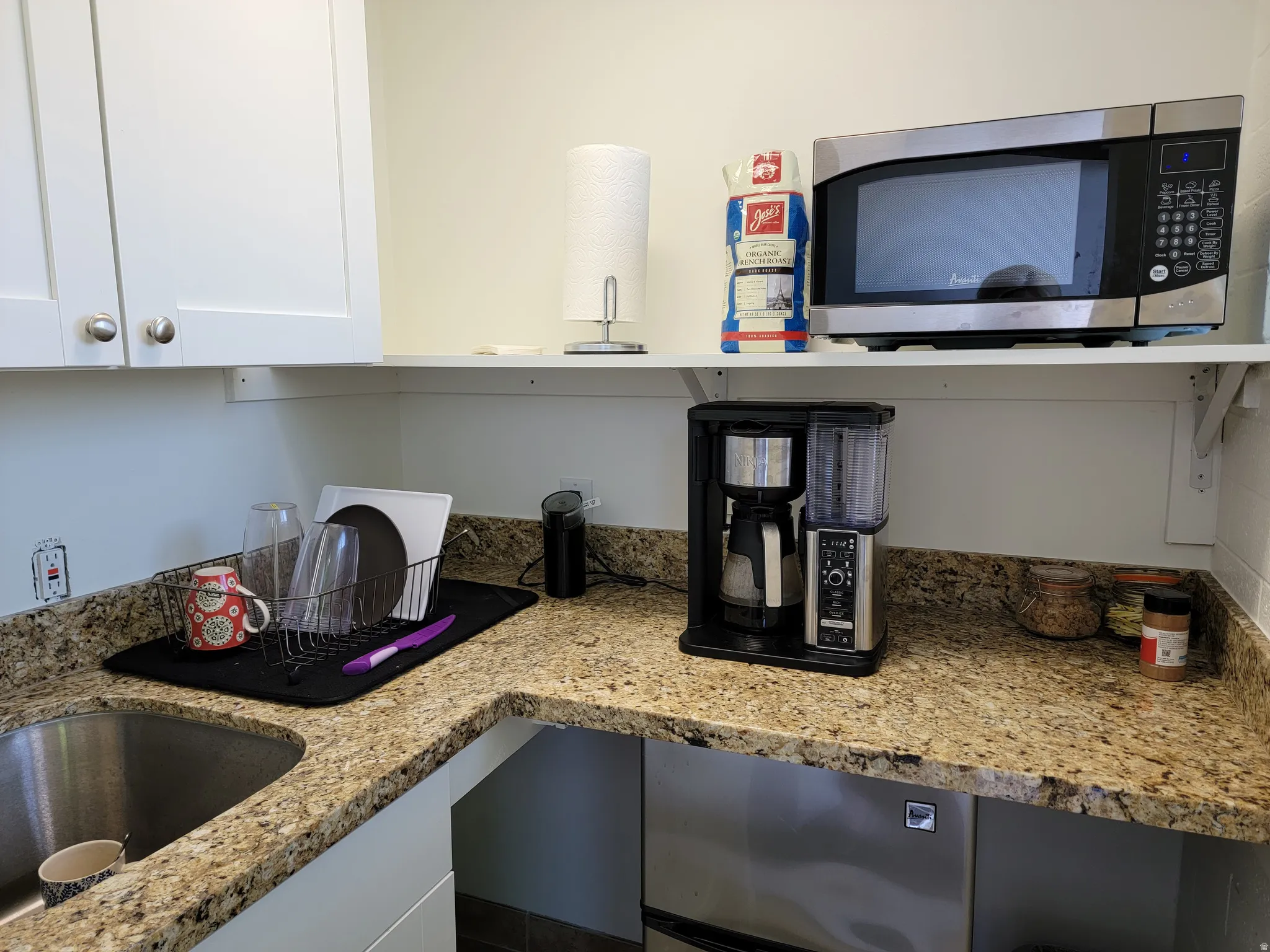 Kitchenette with stainless steel microwave, granite counters, and white cabinetry