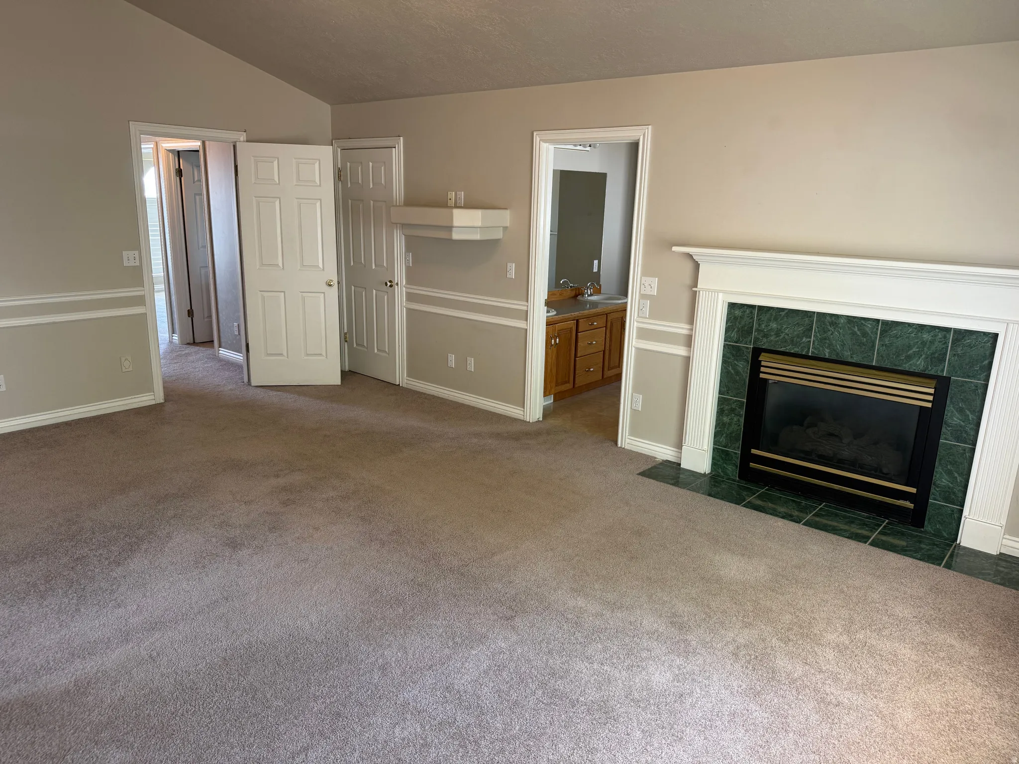 Furniture removed from Master Bedroom area featuring a fireplace with a white mantel and green tile surround, neutral carpeting, and chair rail molding