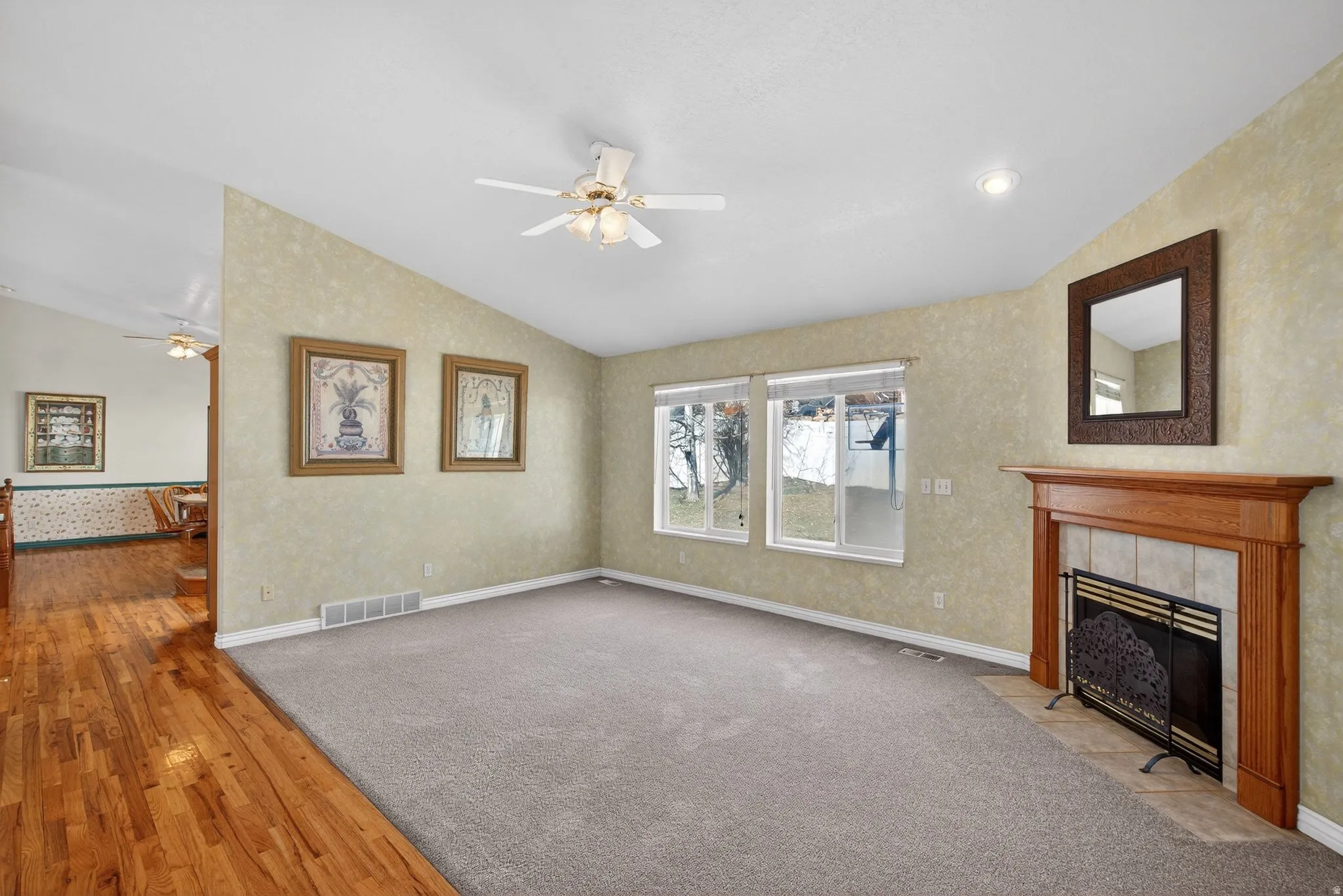 Unfurnished living room with ceiling fan, light wood-style floors, lofted ceiling, a tile fireplace, and wallpapered walls