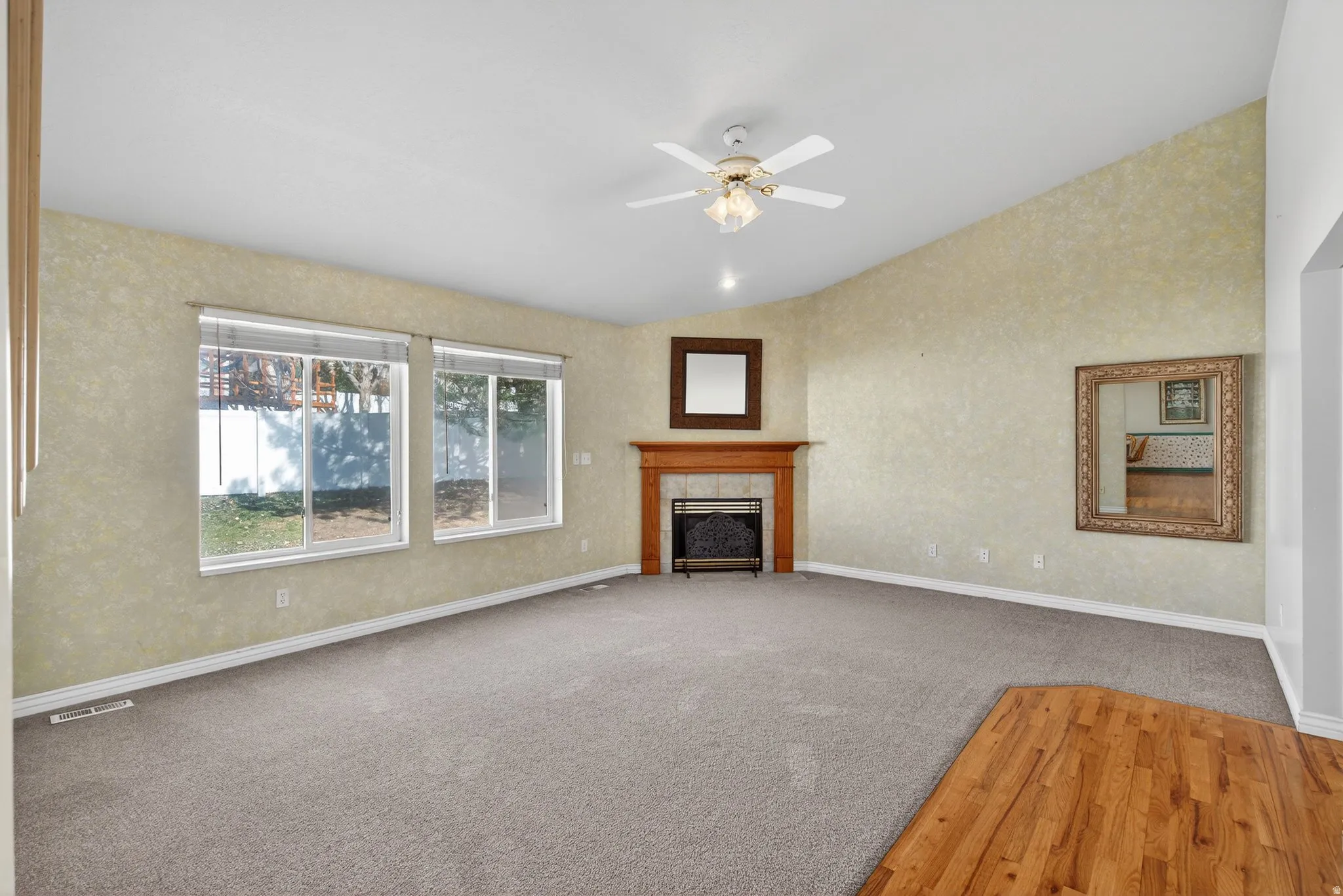Unfurnished living room featuring hardwood / wood-style floors, a ceiling fan, lofted ceiling, a fireplace, and carpet