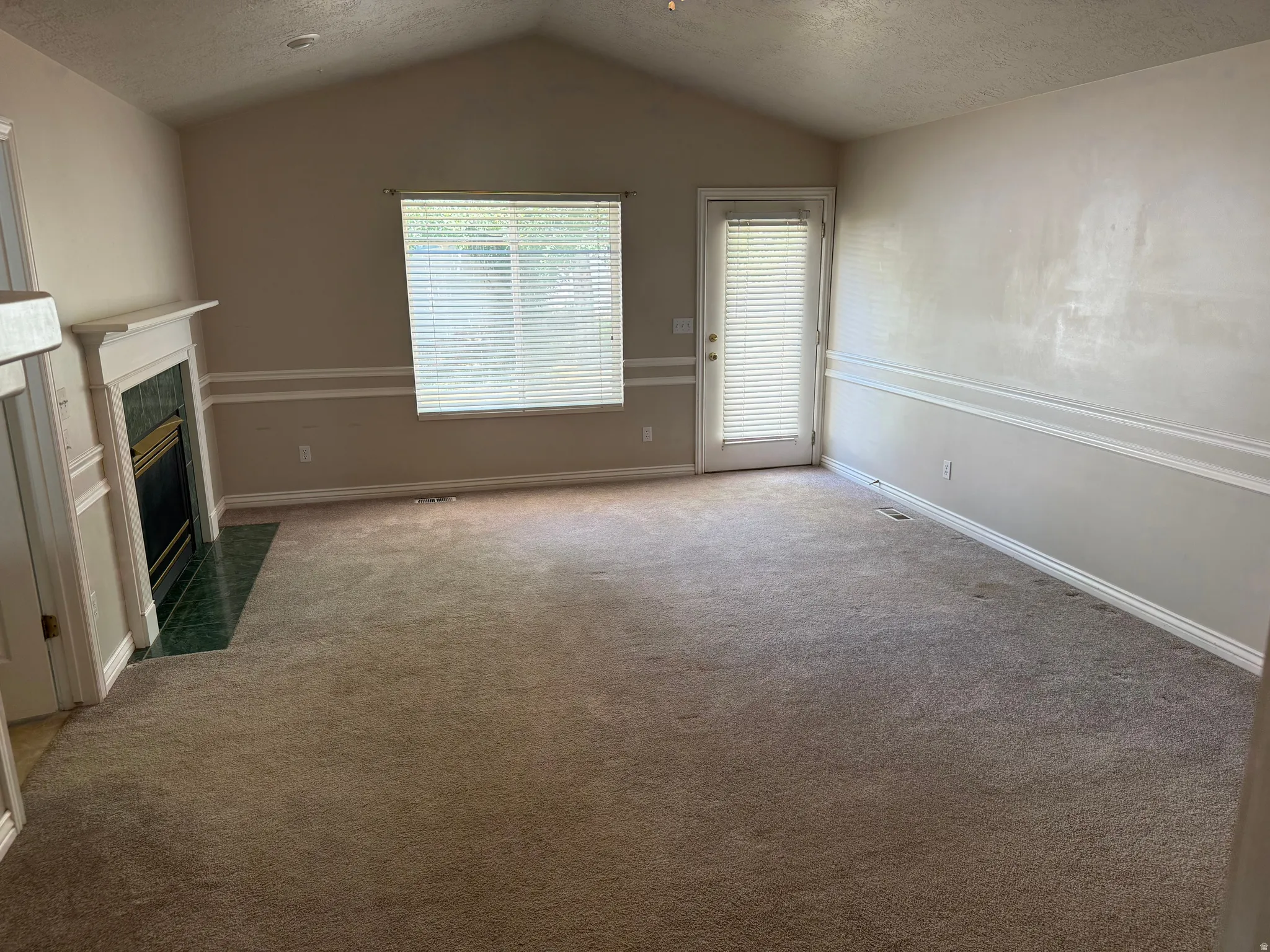 Furniture removed from Master Bedroom  featuring vaulted ceilings, a fireplace with a white mantel and green hearth, carpet flooring, and a glass-paneled door