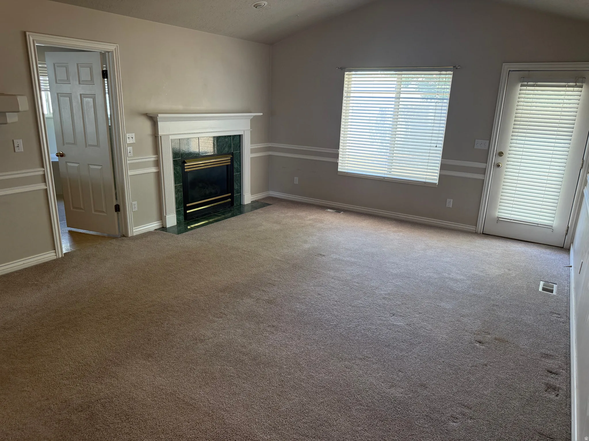 Furniture removed from Master Bedroom featuring vaulted ceilings, a fireplace with a green-veined surround and white mantel, carpeting, a window with blinds, and a white exterior door