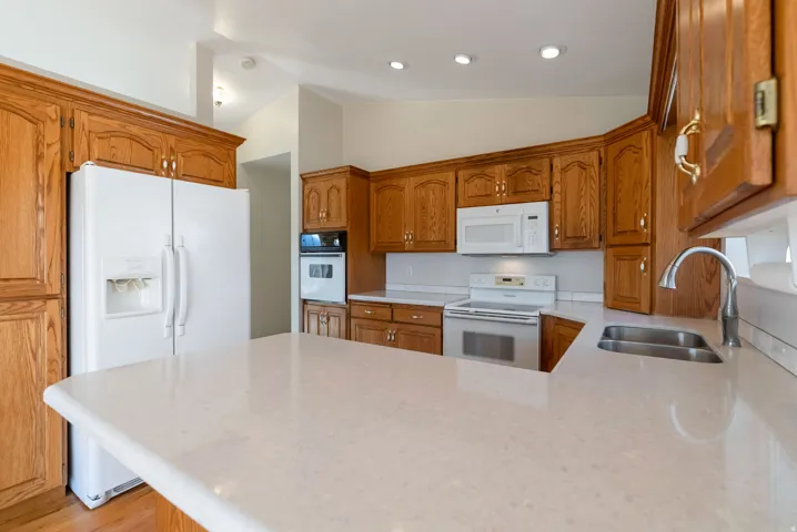 Kitchen featuring wood finish cabinets, white appliances, vaulted ceiling, a peninsula, and light counters
