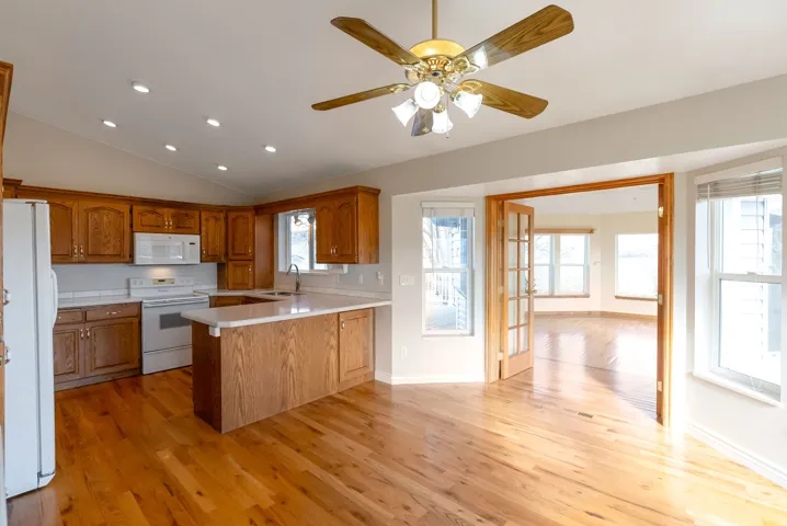 Kitchen with light countertops, wood finish cabinets, white appliances, a peninsula, and lofted ceiling