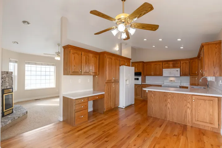 Kitchen with a peninsula, light countertops, wood finish cabinetry, a ceiling fan, and white appliances