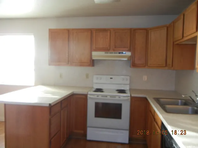 Kitchen featuring white electric stove, a peninsula, light countertops, and wood finish cabinets