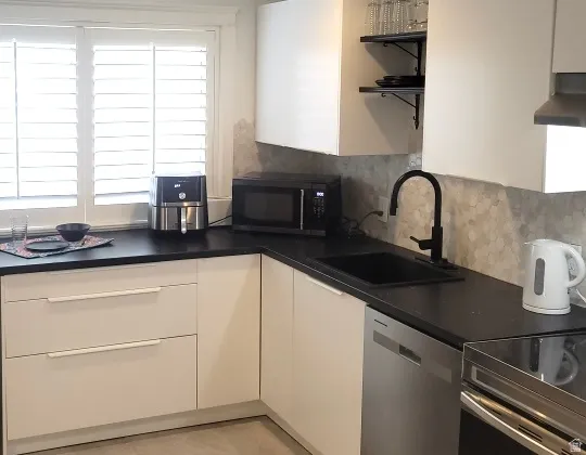 Kitchen featuring stainless steel appliances, dark countertops, white cabinets, and backsplash