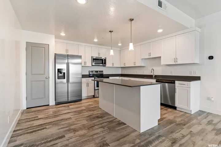 Kitchen featuring stainless steel appliances, dark countertops, a kitchen island, and white cabinets