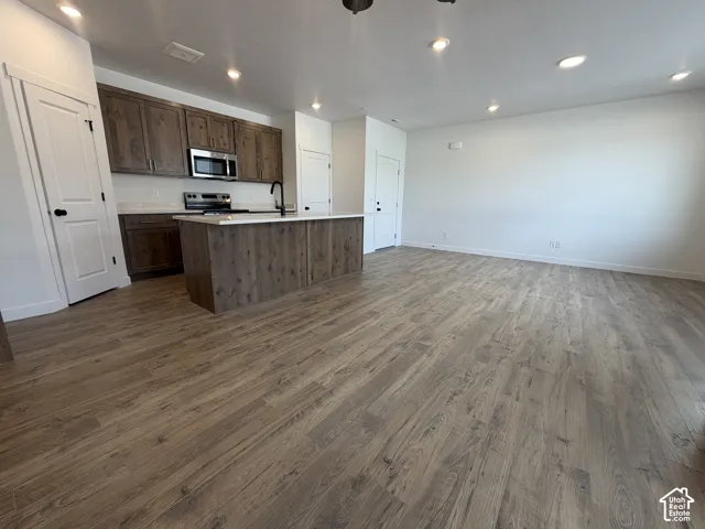 Open-concept living area featuring wood-finish flooring, recessed lighting, a kitchen island with a white countertop, and dark wood cabinetry