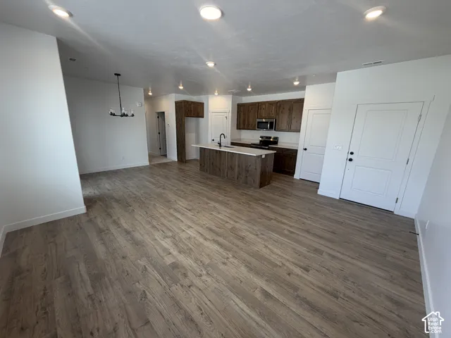 Open-concept living area featuring wood-finish flooring, recessed lighting, a kitchen island with a white countertop, dark wood-finish cabinetry, and a modern chandelier
